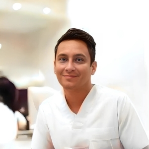 Dr Jorge amaya with short black hair and in white scrubs smiling at the camera